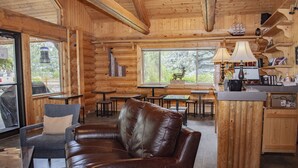 A cozy cabin interior with a leather sofa, wooden tables, and a kitchen area. - Bonners Ferry Log Inn (Bonners Ferry)