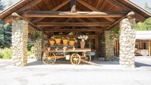 A rustic wooden pavilion with stone pillars, a wooden bench, and a cart with potted plants. - Bonners Ferry Log Inn (Bonners Ferry)