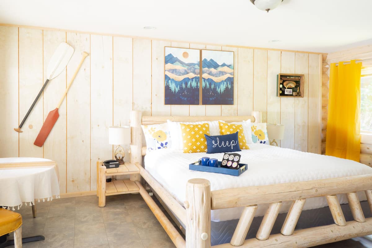 A wooden-framed bed with a white bedspread, a tray with items, and a painting above it.