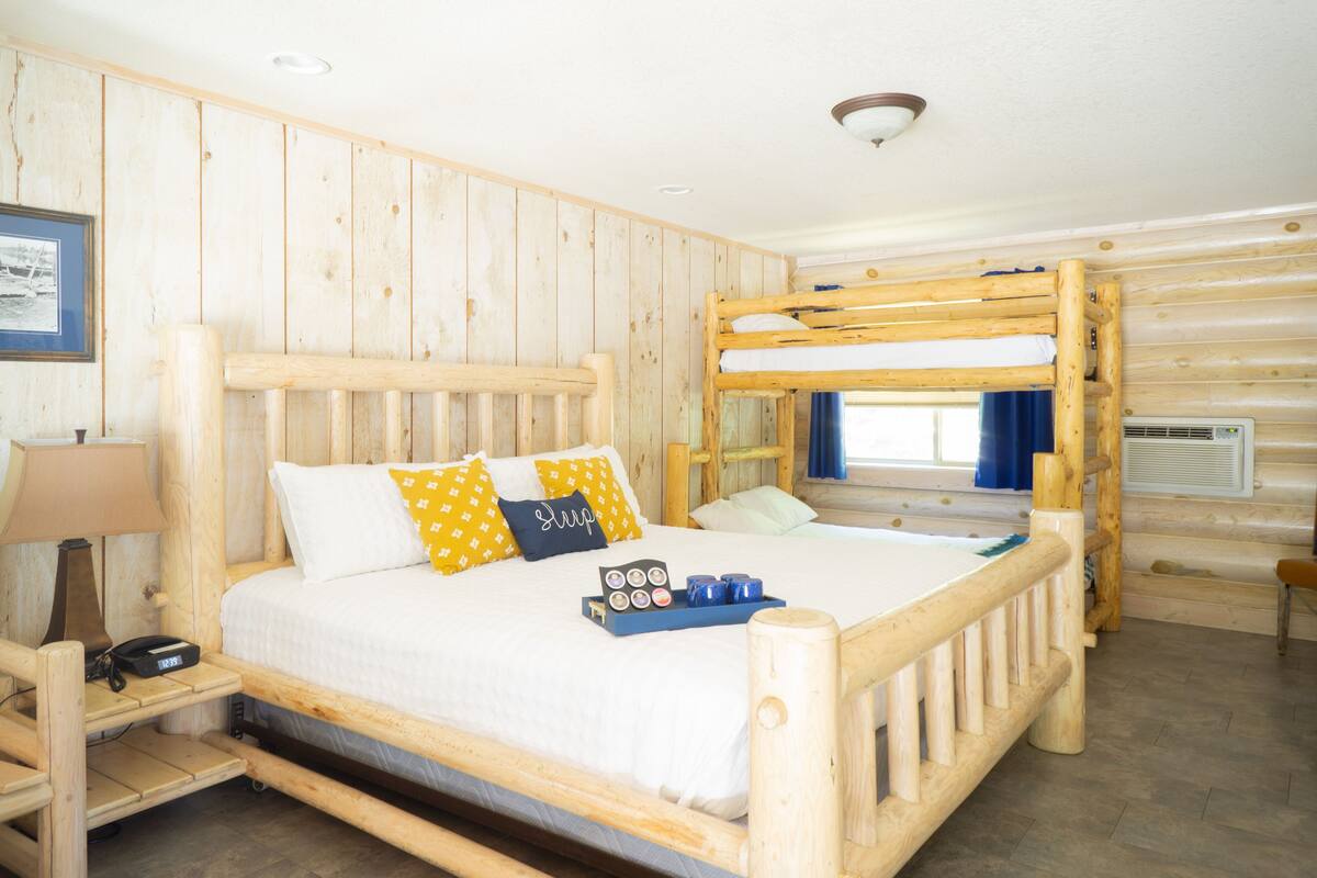 A wooden bunk bed room with a bedside table, a lamp, and a tray with cups and a box.