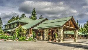 A lodge with a green roof, stone pillars, and a porch with outdoor seating. - Bonners Ferry Log Inn (Bonners Ferry)