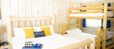Een slaapkamer met een houten stapelbed, een wit bed, een dienblad met bekers en een houten hoofdbord.