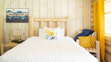 A wooden cabin bedroom with a bed, pillows, a nightstand, a lamp, and a painting on the wall.