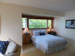 A bedroom with a bed, two bedside tables, a nightstand, a window with a view of trees, and a wall-mounted TV.