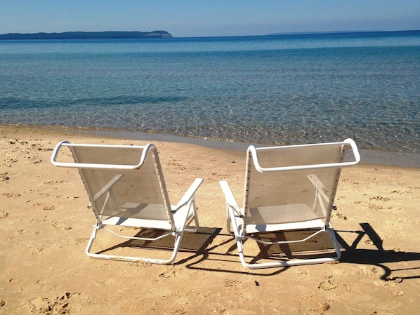 Two beach chairs facing the sea with a clear view of the shoreline and distant land.