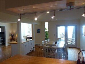 A modern kitchen with white cabinets, a wooden dining table, and a view of the outdoors through a sliding glass door.