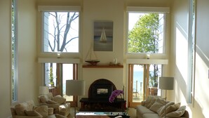 A spacious living room with large windows, a fireplace, and a view of the sea. - Good Harbor Bay Estate, Lake Michigan (Lake Leelanau)
