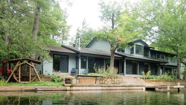 A lakeside cabin with a dock, a swing set, and a covered patio area. - The Weaver House (Glen Arbor)