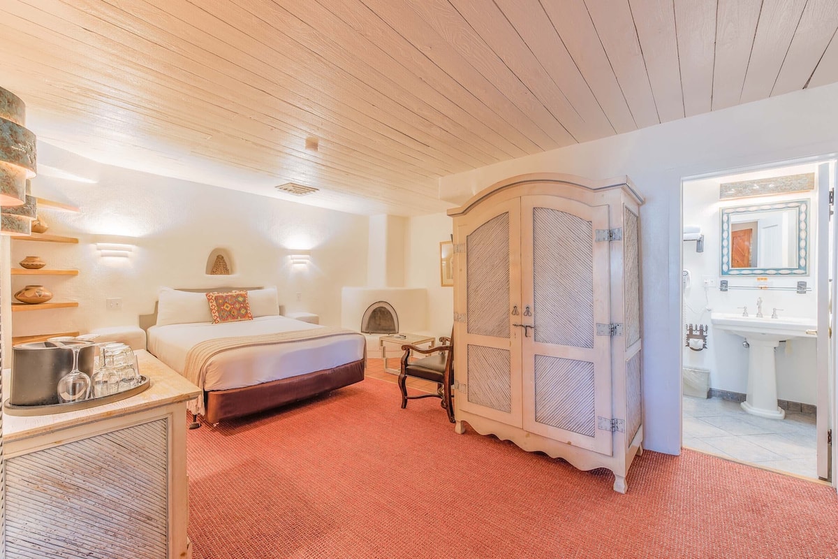 A room with a bed, a dresser, a cabinet, a fireplace, and a bathroom with a sink and mirror.