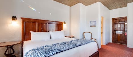 A hotel room with a wooden headboard, a large bed with a patterned bedspread, a small round table, and a door with a sign.