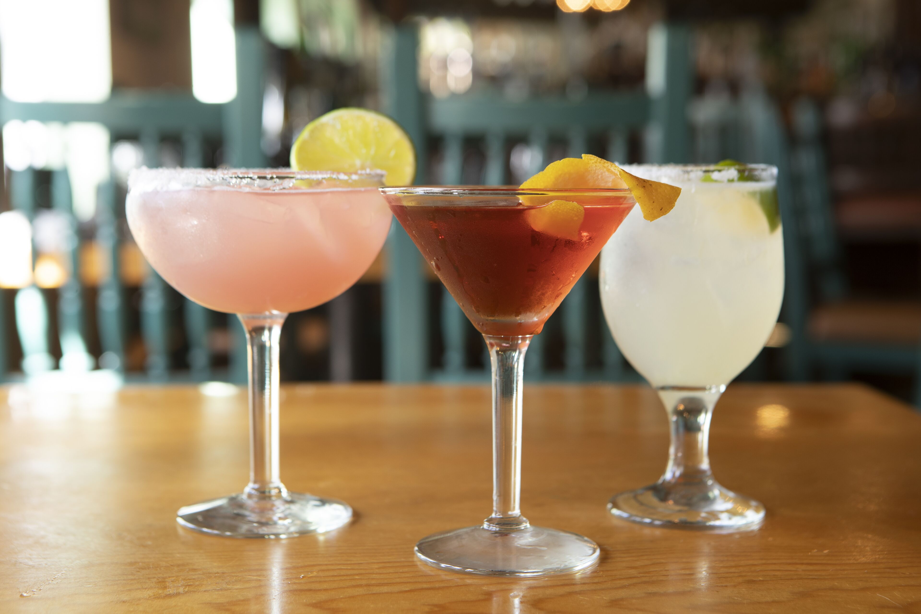 Three cocktails on a wooden table with a blurred background.