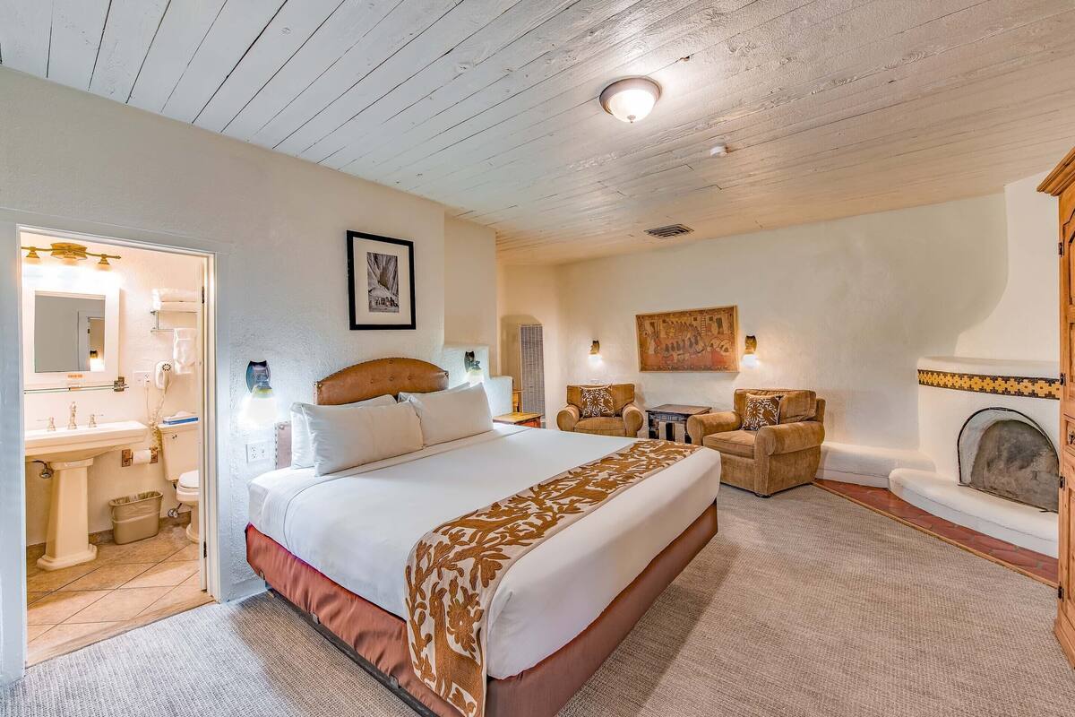 A spacious bedroom with a large bed, a sitting area with a fireplace, and a bathroom with a sink and toilet.