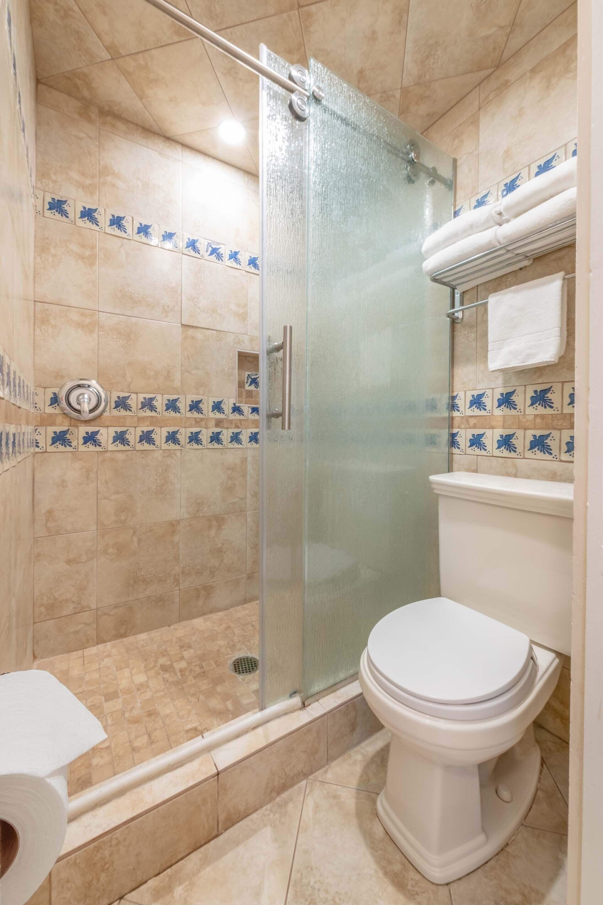 A bathroom with a glass-enclosed shower, a toilet, and a sink.