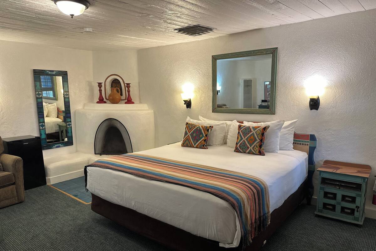 A hotel room with a large bed, a fireplace, a mirror, and a small side table.