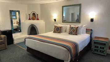A hotel room with a large bed, a fireplace, a mirror, and a small side table.