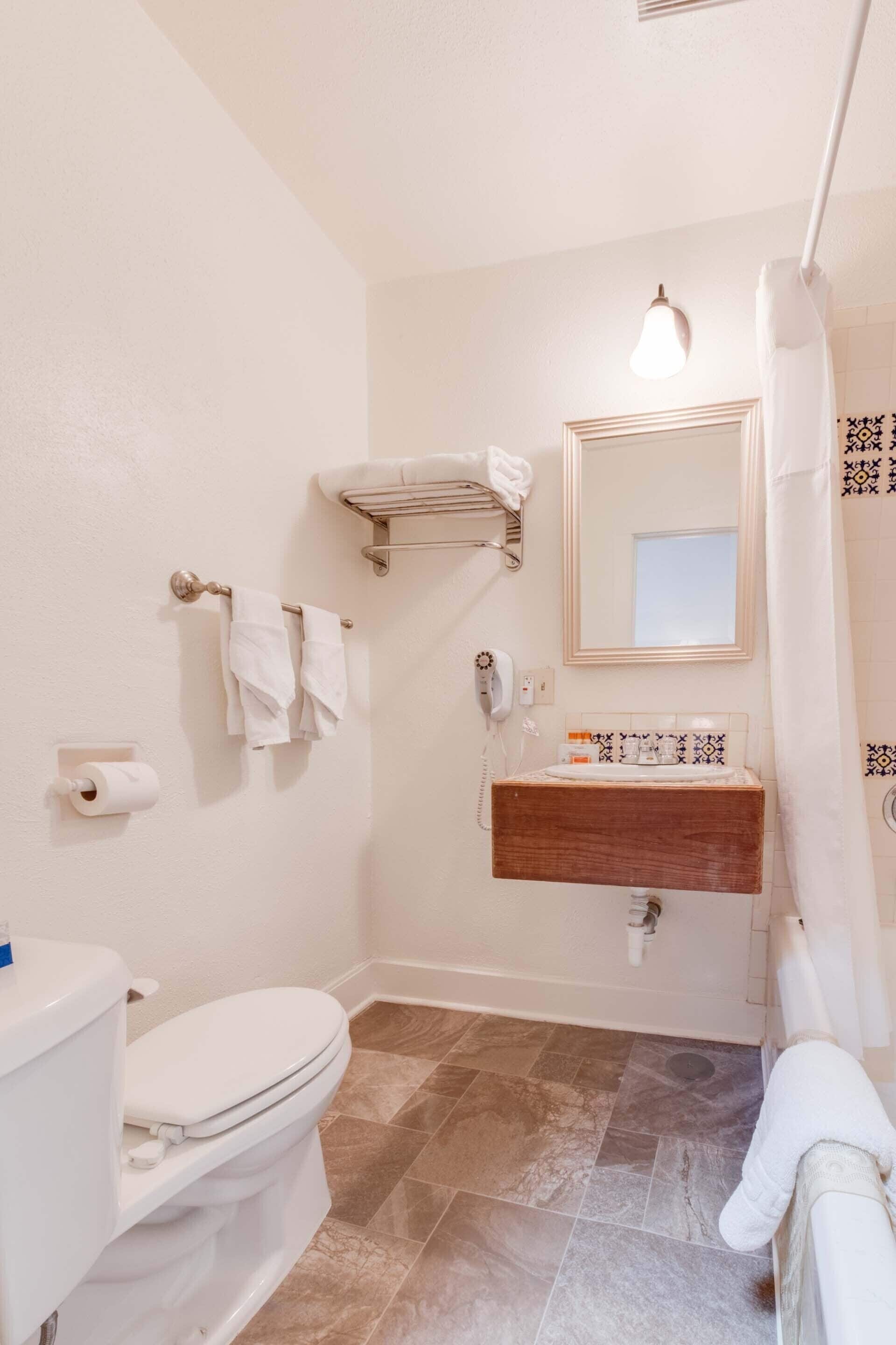 Un baño con inodoro, lavamanos, espejo, toallero y cortina de ducha.