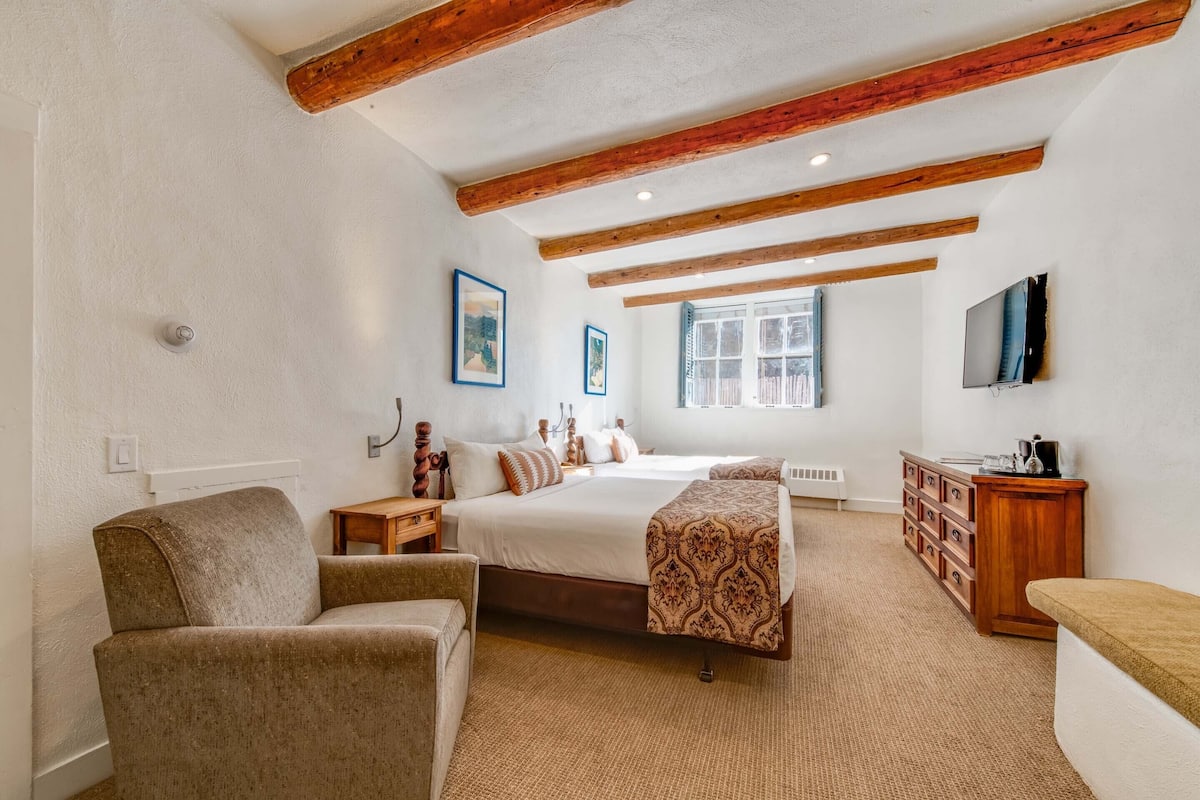 A bedroom with a large bed, wooden beams, a TV, and a dresser.