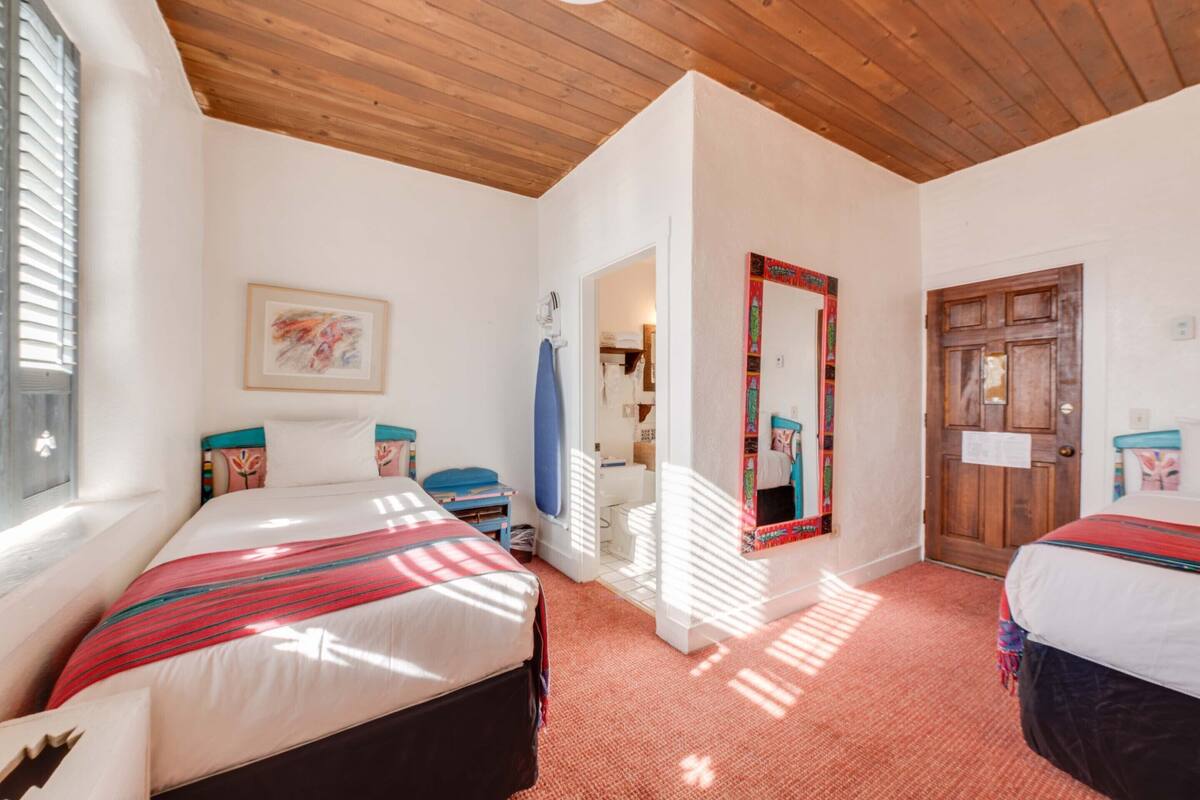 A bedroom with two beds, wooden ceiling, white walls, and a door with a mirror.