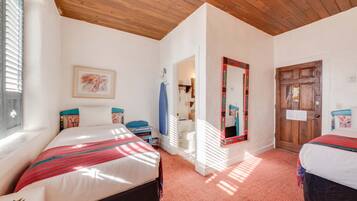 A bedroom with two beds, wooden ceiling, white walls, and a door with a mirror.