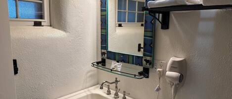 A bathroom with a white sink, a mirror with a decorative frame, a towel rack with a towel, and a hairdryer on the wall.