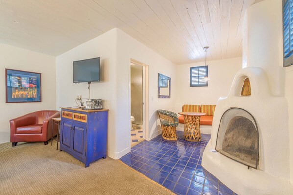 A living room with a blue tiled floor, a fireplace, a television, a sofa, and a red armchair. - The Historic Taos Inn (Taos)