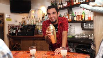 A bar with a bartender preparing drinks. There are multiple bottles and glasses on shelves behind the bartender.