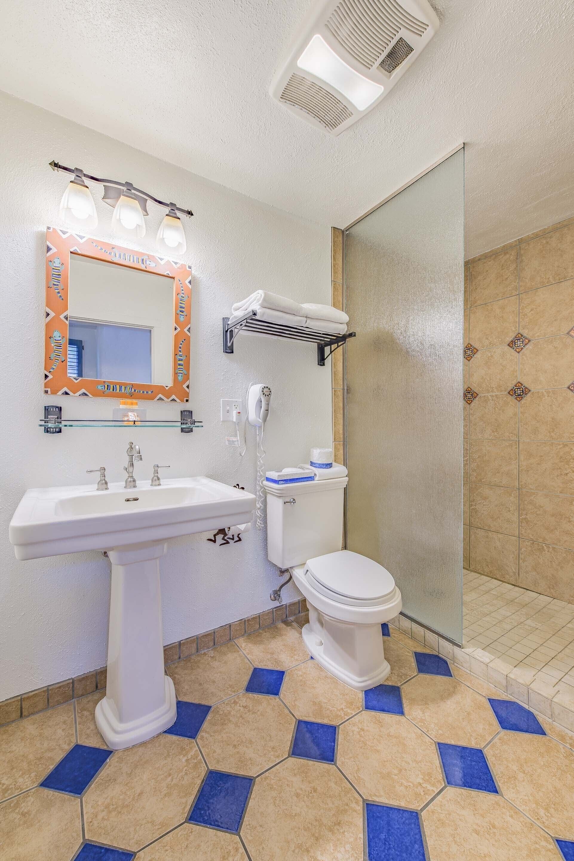 A bathroom with a pedestal sink, a toilet, a glass shower enclosure, and a vanity mirror with lights.