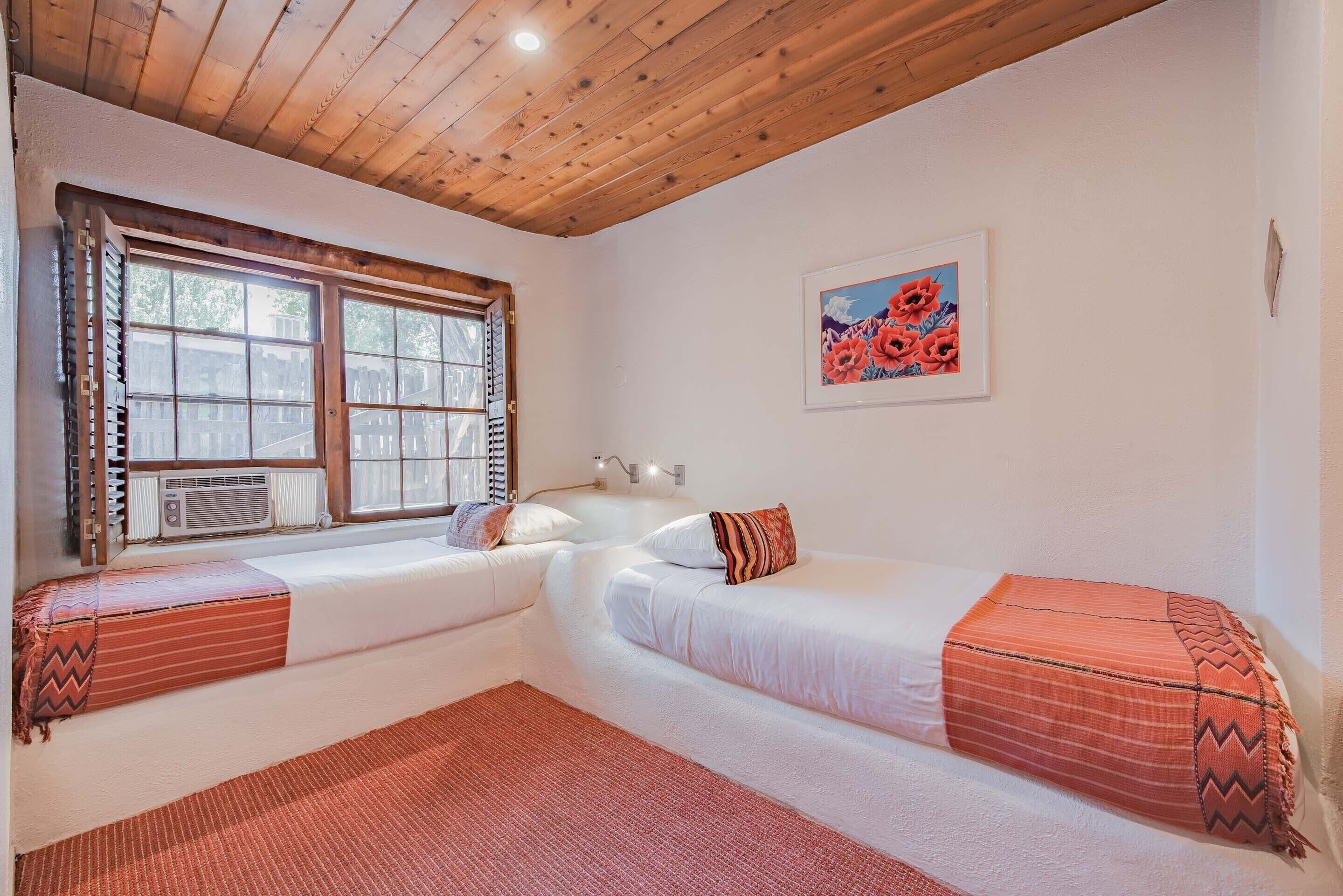 Een kamer met twee bedden, een raam met zonwering, een radiator en een schilderij aan de muur.