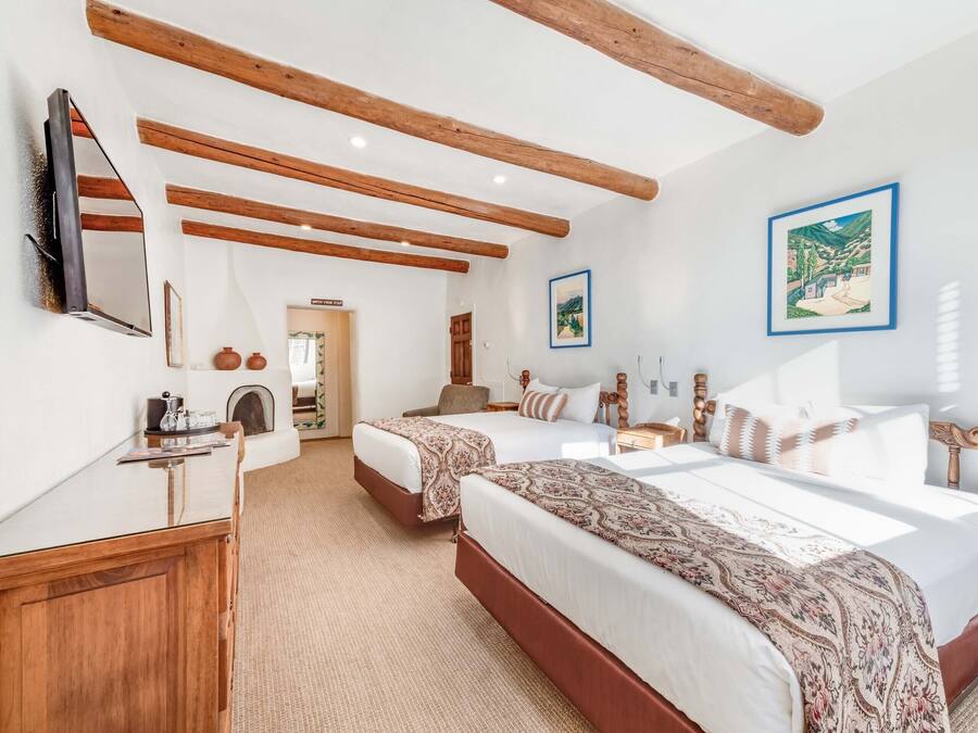 Ein Hotelzimmer mit zwei Betten, Holzbalken an der Decke, einem Flachbildfernseher und einem gerahmten Bild an der Wand.
