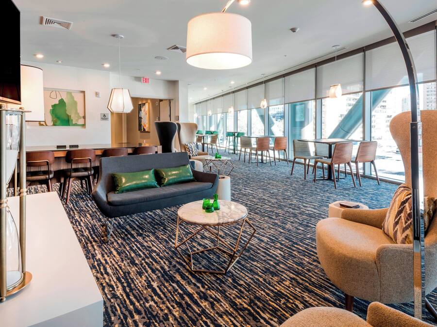 En modern hotellobby med en soffa, fåtölj, runt soffbord och en matplats med stolar och ett bord.