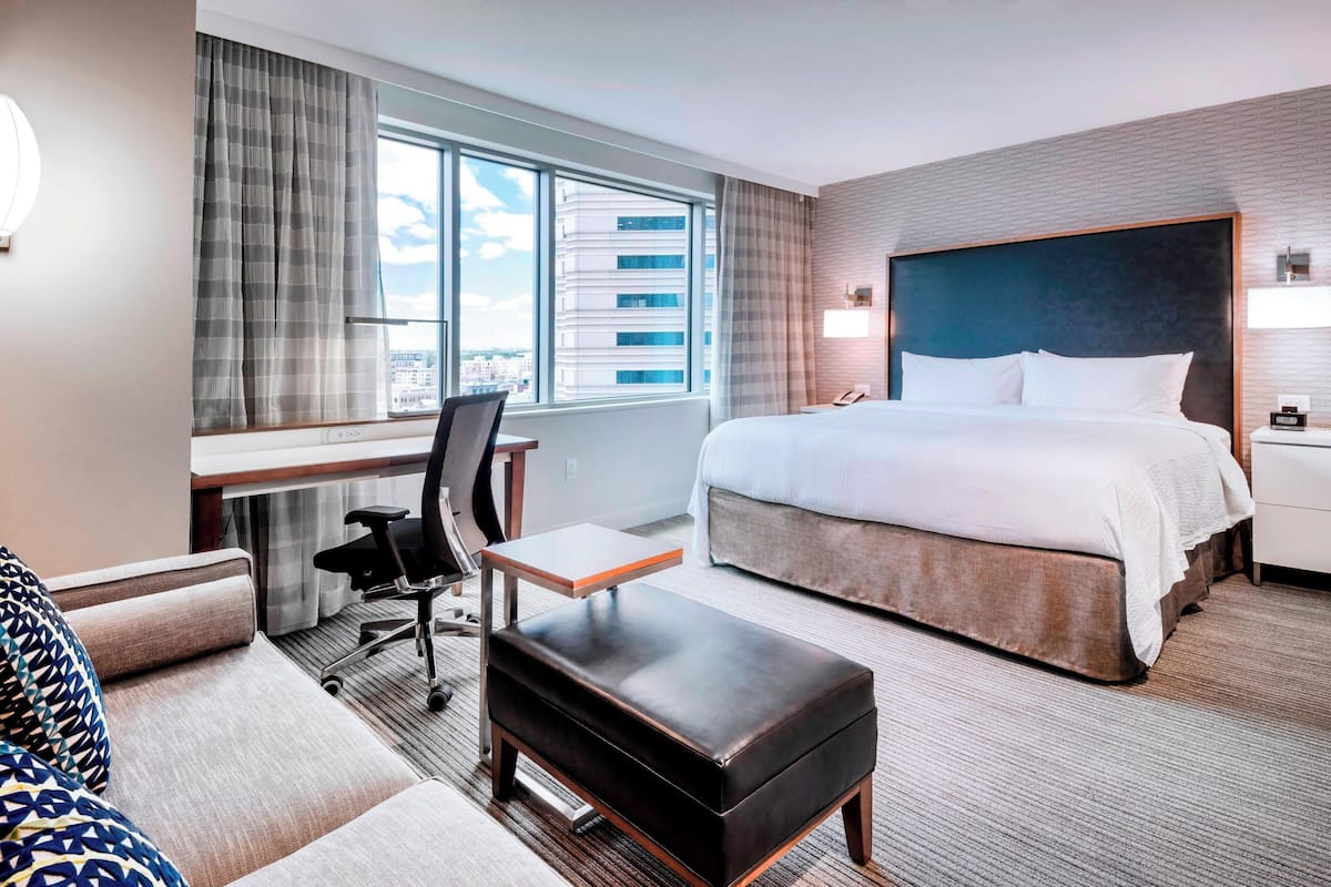 A hotel room with a large bed, a desk with a chair, a small table, and a sofa.