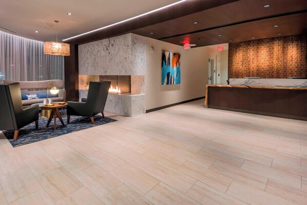 A modern lobby with a reception desk, seating area with chairs and a table, a fireplace, and a large abstract painting on the wall. - Residence Inn by Marriott Jersey City (Jersey City)