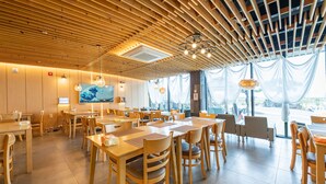 A spacious restaurant with wooden tables and chairs, a high ceiling with wooden slats, and large windows with sheer curtains. - Sky Hotel (Jeju City)