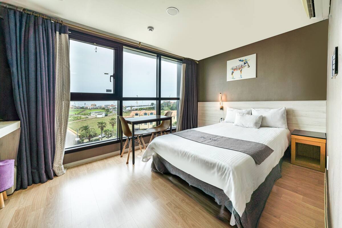 Ein Hotelzimmer mit einem großen Bett, einem Schreibtisch und Blick auf die Stadt.