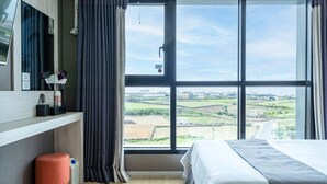 A bedroom with a large window, a bed, a TV, and a small stool. - Sky Hotel (Jeju City)