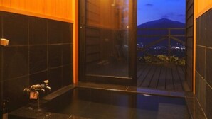 Ein modernes Badezimmer mit einer großen Badewanne, dunklen Fliesen und Blick auf eine Stadtlandschaft im Abendlicht.