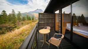 Ein Balkon mit Holztisch und -stühlen, ein Bett mit weißer Bettwäsche und Blick auf die Berge.
