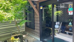 Ein modernes Gebäude mit Glastür, ein kleiner Garten mit Baum und verschiedene Schilder, darunter ein PayPay-Schild.