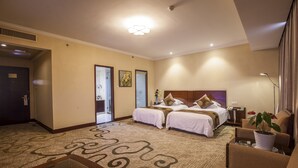 A hotel room with two beds, a large window, a carpeted floor, and a desk with a lamp.