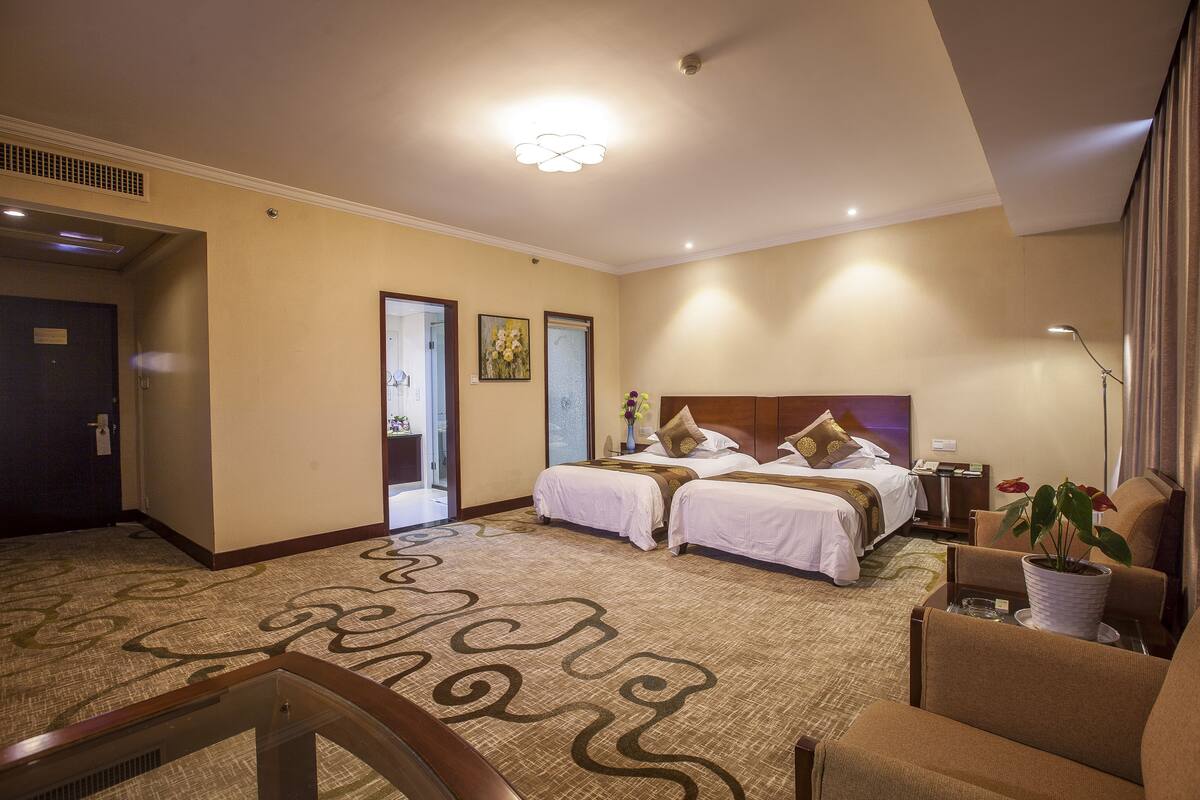 Ein Hotelzimmer mit zwei Betten, einem großen Fenster, einem Teppichboden und einem Schreibtisch mit Lampe.