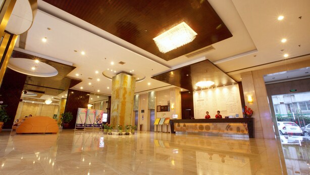 A modern hotel lobby with a reception desk, seating area, and a large chandelier.