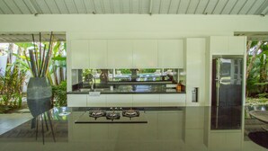 A modern kitchen with a gas stove, white cabinets, and a large vase of plants. - Villa Senara (Canggu)
