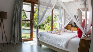 A bedroom with a bed under a canopy, a tripod lamp, and a view of greenery outside. - Villa Senara (Canggu)