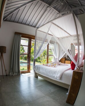 A bedroom with a bed under a canopy, a tripod lamp, and a view of greenery outside. - Villa Senara (Canggu)
