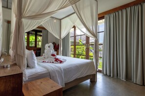 Habitación de hotel con cama a dosel, cabecera de madera y vistas a zonas verdes.