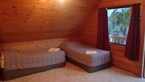 Ein kleiner, gemütlicher Raum mit zwei Betten, einem Fenster mit Vorhängen und einer Holzbalkendecke.