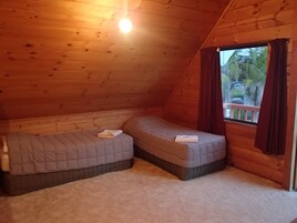 Um quarto pequeno e acolhedor, com duas camas, uma janela com cortinas e teto de madeira.