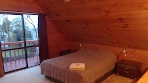 Ein Schlafzimmer mit Bett, Nachttisch, Holzkommode und einer Schiebetür zu einer Terrass'.