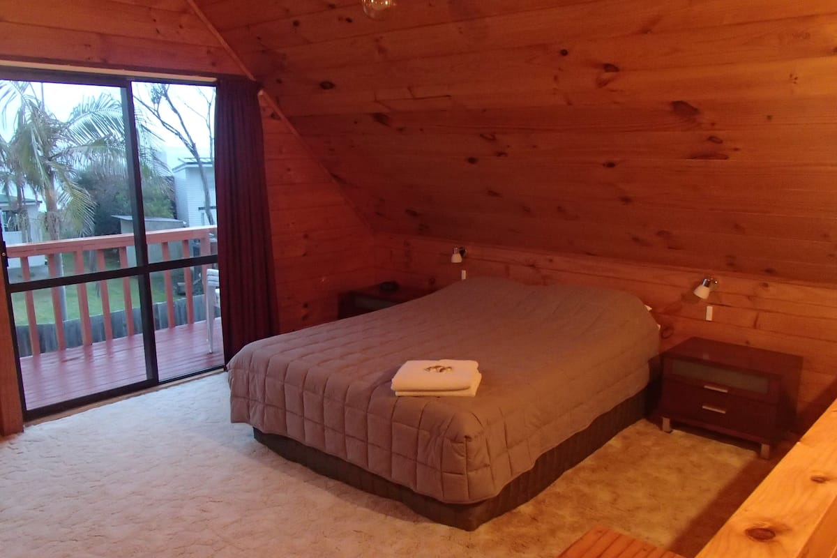 Un dormitorio con cama, mesita de noche, cómoda de madera y puerta corrediza de vidrio que da a una terraza exterior.
