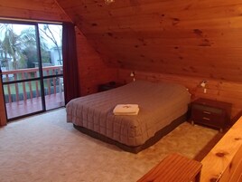 Quarto com cama, mesa de cabeceira, cômoda de madeira e porta de vidro corria para um deck exterior.